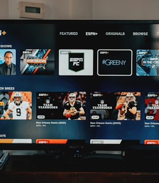 A television screen displaying the ESPN+ streaming interface with various sports-related shows and categories. The screen includes sections such as 'Browse by Shows' and 'Best of Drew Brees' with thumbnails of sports programs featuring athletes in action and analysts.