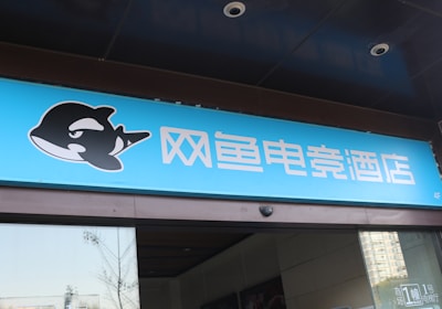 A building entrance features a vibrant blue sign with white Chinese characters and a stylized orca logo in black and white. The overall appearance suggests an establishment focused on eSports or digital activities.